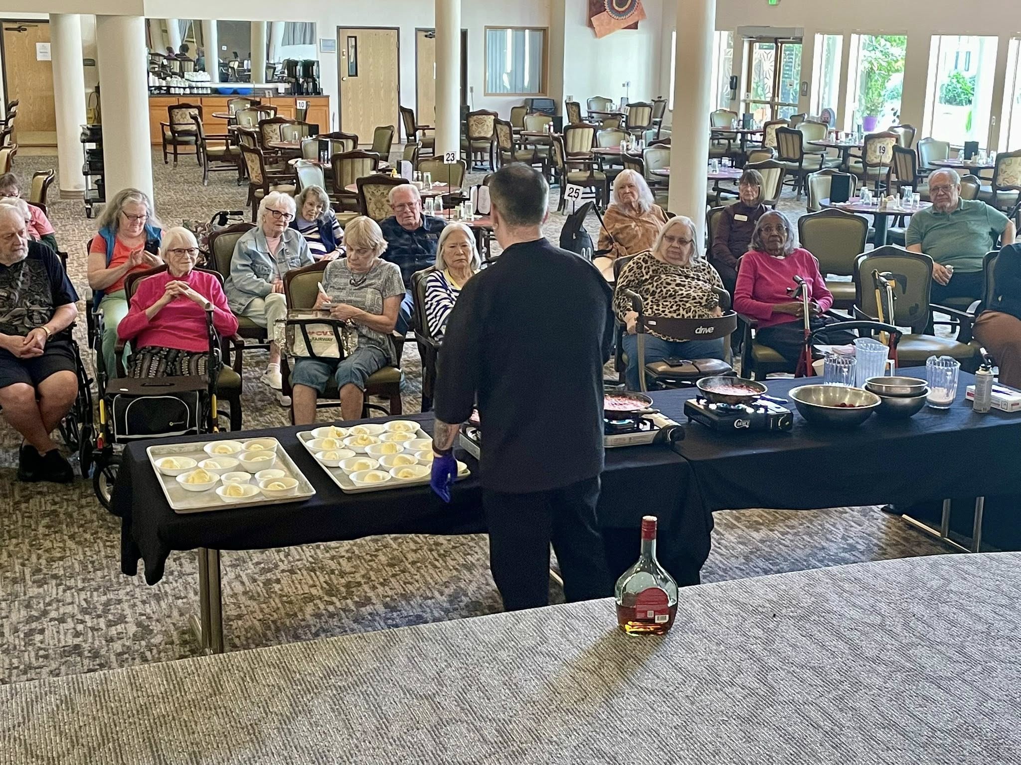 Interactive Culinary Program — Residents clapping at a live chef demonstration in the dining room.